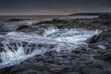 Dramatic coastal scene in Gran Canaria with waves crashing against dark volcanic rocks. El Bufadero