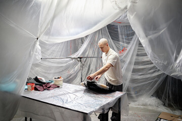 Shot through masking film covering surfaces of workshop where male fashion artist working on...