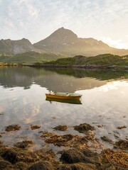A boat at sunset on a tranquil fjord surrounded by mountains. 