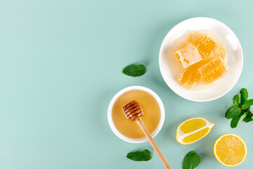 Acacia honey, honeycomb, lemon and mint leaves on blue background. Top view. Copy space.