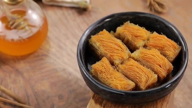 Traditional pastry pieces served in a black bowl with honey jar on a wooden surface, concept of culinary craftsmanship and cultural heritage