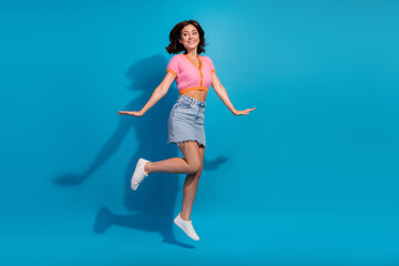 Obraz premium Smiling young woman in casual summer outfit jumps happily against a bright blue background.