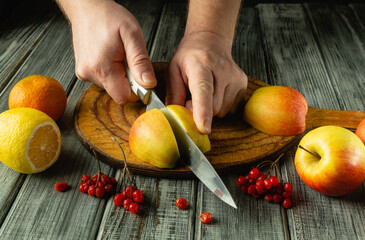Hands deftly slice a ripe apple on a rustic wooden board surrounded by vibrant fruits. The bright...