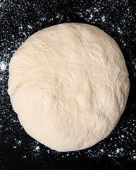 Raw dough for bread or pizza on a black background