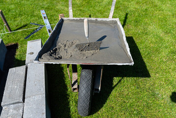A wheelbarrow filled with liquid concrete mixed by hand in a freestanding concrete mixer.