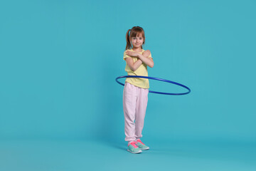 Cute little girl exercising with hula hoop on light blue background