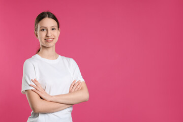 Fototapeta premium Portrait of smiling teenage girl with crossed arms on pink background. Space for text