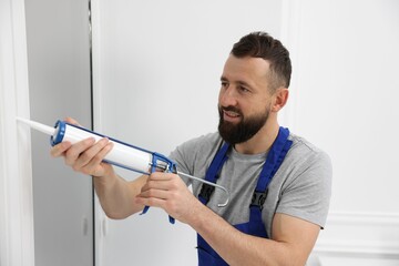 Worker with caulking gun sealing window indoors