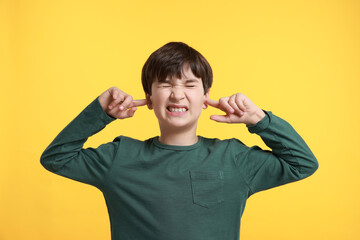 Annoyed boy covering his ears due to loud sound on yellow background