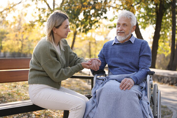 Caregiver assisting senior man on wheelchair in park. Home health care service