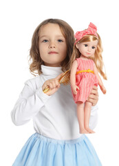 Cute little girl brushing doll's hair on white background