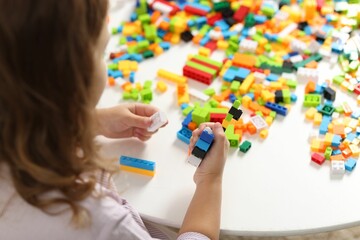 Girl playing with building blocks at white table indoors, closeup