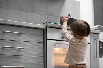 Little boy playing with pot on stove in kitchen, back view. Dangerous situation