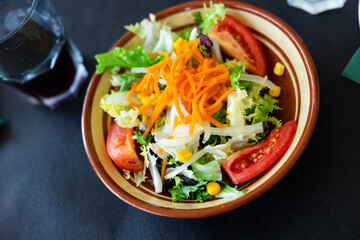 Plate contains portion of salad from fresh China cabbage, grated carrot, corn, tomato complemented by small glass of wine.