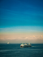 Naklejka premium USA, Washington State, Seattle. Ferry sails into Seattle's Elliot Bay in front of morning fog and the Olympic Mountains.