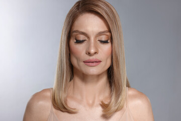 Fototapeta premium Portrait of beautiful woman with straight blonde hair and stylish makeup on light grey background