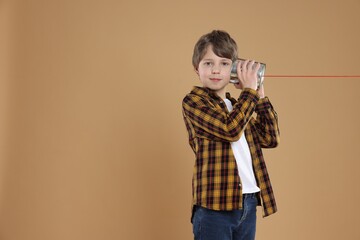 Boy using tin can telephone on beige background. Space for text