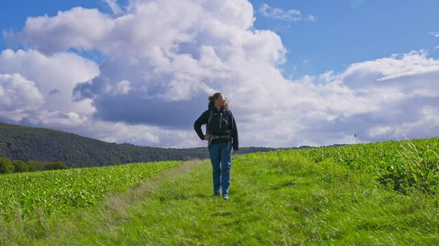 Standing backpacking hiker taking in the lush farmland and grassy meadow before continuing to walk on a partly cloudy summer day, Rhine Valley, Germany