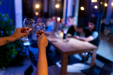Two people clinking glasses of rose wine against a dimly lit gathering backdrop during an evening celebration