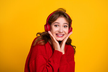 Happy woman wearing red sweater with headphones enjoying music on yellow background