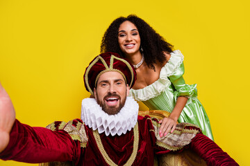 Fototapeta premium Two people dressed as royalty laughing in front of a vibrant yellow background, showcasing historical costumes