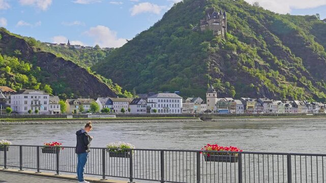 Woman taking a photo of a picturesque town along the Rhine River bank on an early summer morning, St. Goar, Germany