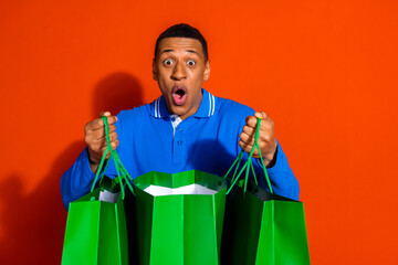 Surprised young man with green shopping bags on vibrant orange background