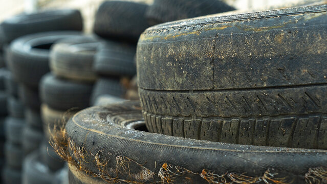 Close-up view of discarded old car tires outdoors, showcasing a pile of used tires ready for recycling. Highlighting environmental concerns and rubber waste management. Defocused background.