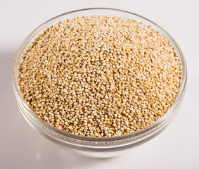 Glass bowl with raw quinoa seeds on white surface. Healthy and nutritious food..