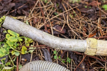 one old dirty gray plastic hose from a vacuum cleaner and a metal tube lies on the ground on the street
