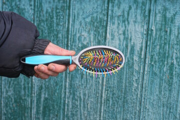  hand in black clothes holding one color plastic hair comb on autumn street against green wall
