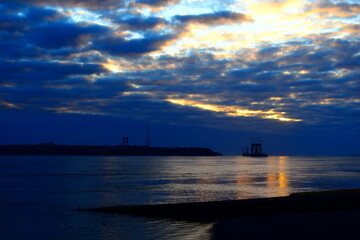 Breathtaking seascape at sunset with a dramatic sky filled with deep blue and golden clouds. The calm water reflects the warm light, creating a peaceful yet mysterious atmosphere. In the distance