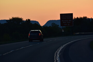 Sunset over an American highway with a road sign and a vehicle. Scenic view, road trip, travel, journey, American landscape, highway, sunset glow, evening drive, adventure, freedom on the road