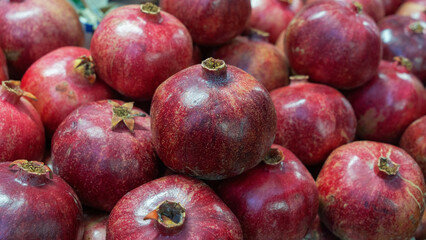 A vibrant close-up of a pomegranate at a bustling market, showcasing its rich red color and textured skin. The blurred background hints at a lively marketplace.