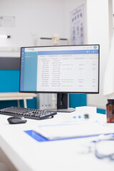 On desk of hospital office, desktop pc is displaying patient doctor appointments as documents, pill bottle, keyboard and mouse are placed nearby. Computer showing use of modern technology in a clinic.