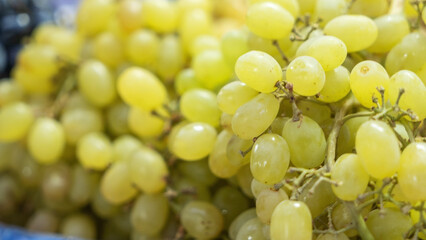 A close-up of a vibrant green grape bunch displayed at a bustling market. The fresh grapes glisten under the light, showcasing their juicy texture and inviting color, perfect for a healthy snack.