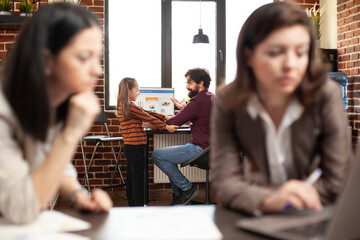 Selective focus on businessman sitting and chatting with little girl brick wall workspace. Working mom and coworker doing research on laptop as her daughter plays with male employee in startup office.