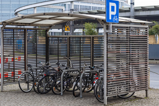 Bicycle parking shelter with multiple bikes locked to metal racks near a modern urban transport hub on a cloudy day. Eco-friendly transport, urban cycling and mobility - Powered by Adobe