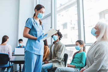 Obraz premium Diverse people sitting in line waiting for their turn to get shots at the hospital vaccination center. Nurse talking with patients in queue for antiviral flu vaccine
