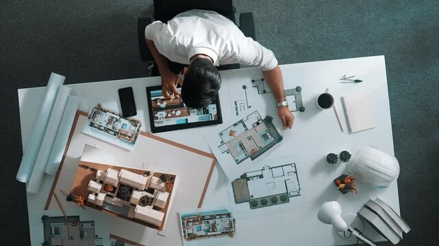 Top view of business man using tablet plan house design while sitting at meeting table with blueprint and equipment scatter around. Aerial view of civil engineer working at blueprint. Alimentation.