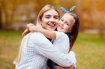 Fototapeta premium Joyful Mother And Daughter Hugging Smiling To Camera Standing In Park Outside. Mom's Love Concept