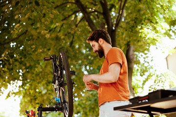 Outdoorsy male cyclist seen in yard inspecting bike for damages to repair and adjust. Athletic dedicated caucasian man carefully examining his modern bicycle for further maintenance.
