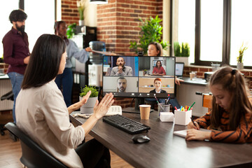 Busy mother participates in videocall with coworkers, presenting business project as her child is drawing in workplace. White woman attends virtual meeting and keeps daughter engaged in creative work.