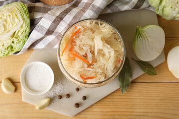 Delicious sauerkraut in jar with ingredients on wooden background. Top view