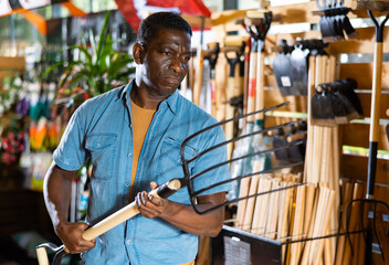 Portrait of african american man choosing pitchfork in gardening market