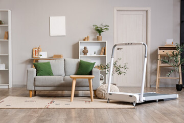 Interior of light living room with treadmill and sofa