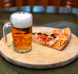 trozo de pizza con cerveza sobre una tabla redonda de madera
