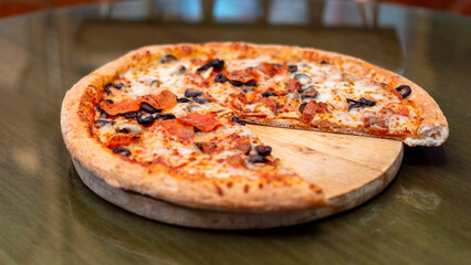 Pizza de pepperoni con aceitunas y champiñones menos un trozo sobre una tabla redonda de madera 