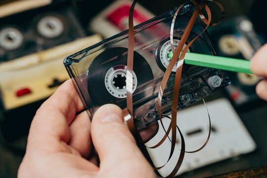 Rewinding magnetic tape in a cassette manually with a pencil, closeup. Old methods of rewinding music tapes, vintage style. Man rewind a cassette tape