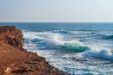 A dynamic seascape with waves colliding against sharp cliffs. The white foam and deep blue water create a dramatic contrast, showcasing the untamed power of the sea.